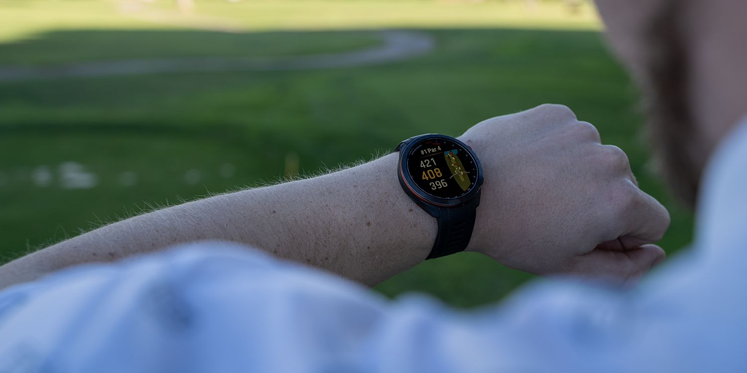 A person is looking at a smartwatch displaying golf data, including hole, par, and distance, on an outdoor golf course.