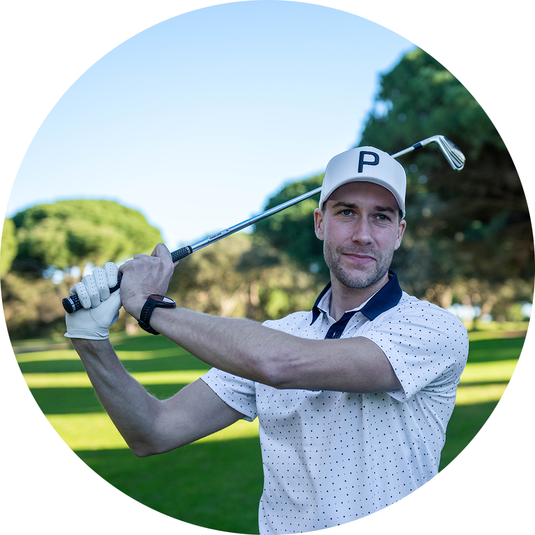 Man i vit keps och golfhandske svingar en golfklubba på en grön golfbana med träd i bakgrunden.