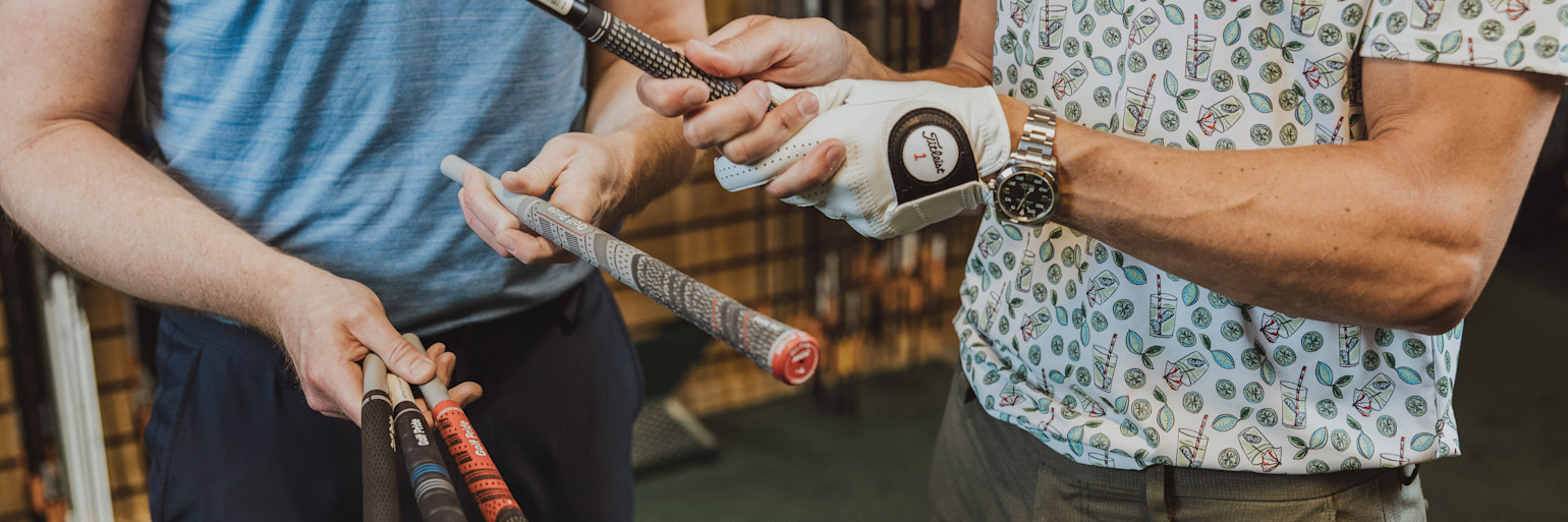 Två personer håller och jämför golfklubbor, en med golfhandske och klocka, i en butiksmiljö.