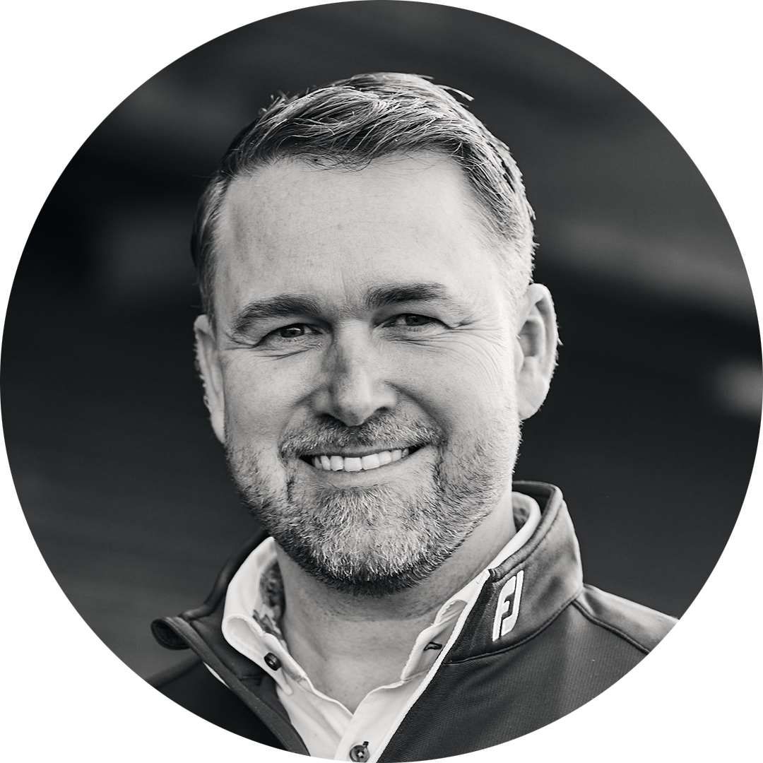 Leende man med kort hår och skägg bär en jacka med FJ-logotyp, suddig bakgrund.