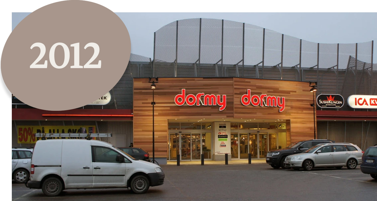 The facade of the Dormy shop with cars parked in front, signs for SushiKungen and ICA Kvantum, and the text "2012" in a circle.