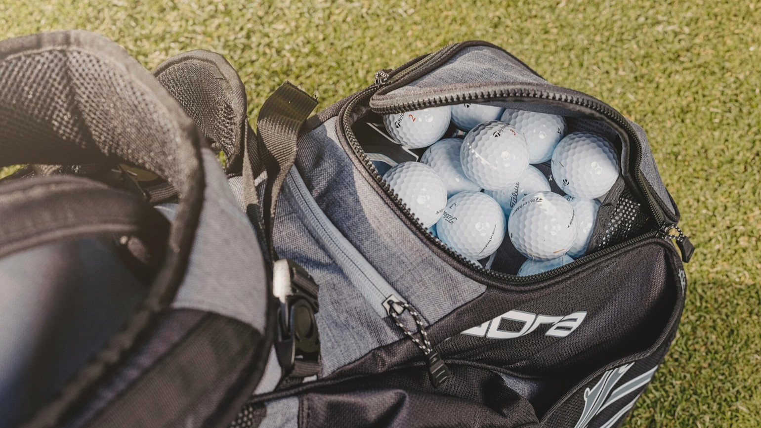 An open golf bag with several white golf balls visible in a compartment, placed on grass.