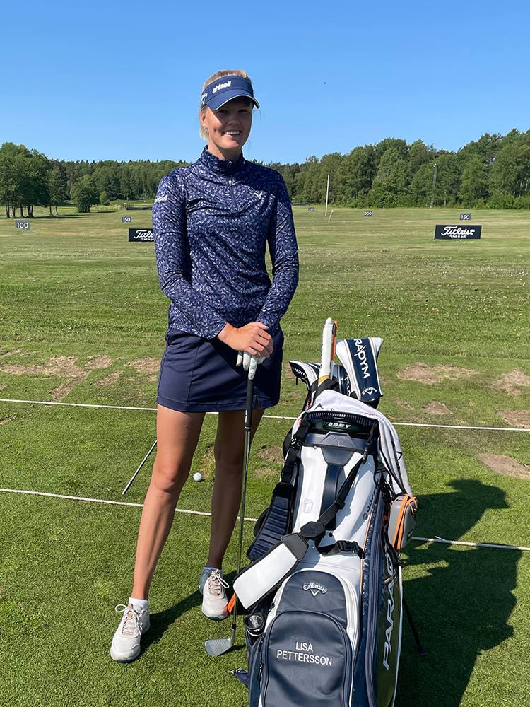 Kvinna i golfkläder står leende bredvid en golfbag märkt "Lisa Pettersson" på en golfbana under klarblå himmel.