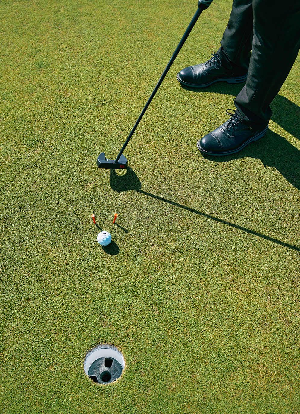 Golfspelare står redo att putta en golfboll mot hålet på greenen, med två peggar bredvid bollen.