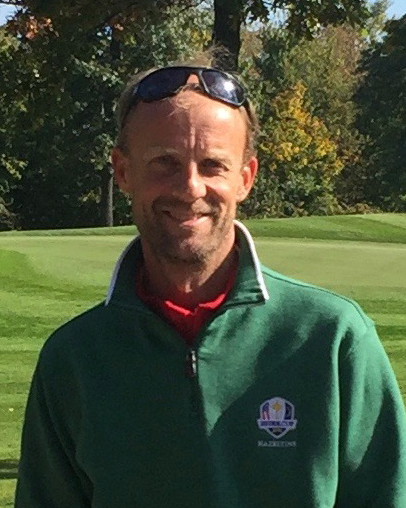 Man med solglasögon på huvudet står utomhus på en golfbana, bär grön tröja med Ryder Cup-logotyp.