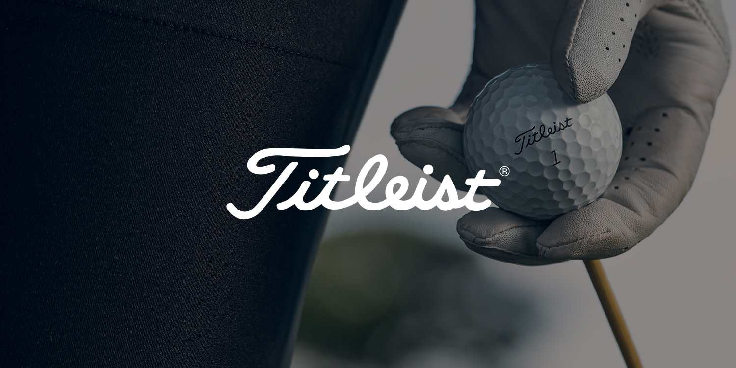 En hand med golfhandske håller en Titleist-golfboll ovanpå en pegg, med Titleist-logotypen i förgrunden.