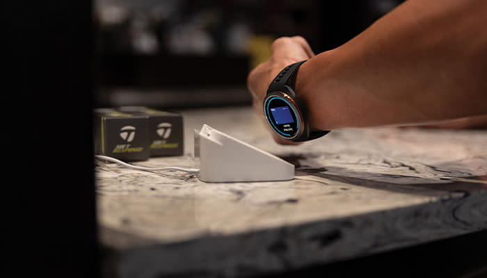 En person håller sin smartklocka mot en kortterminal på en marmordisk för att genomföra en betalning.