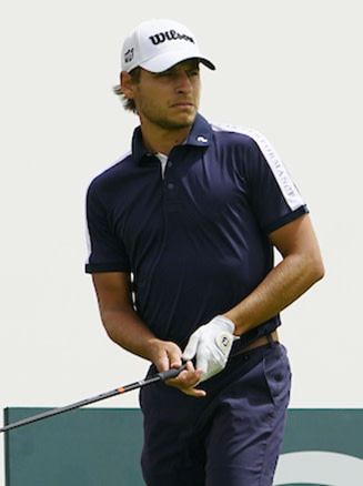 Manlig golfspelare i mörkblå pikétröja och vit keps svingar en golfklubba på en golfbana.