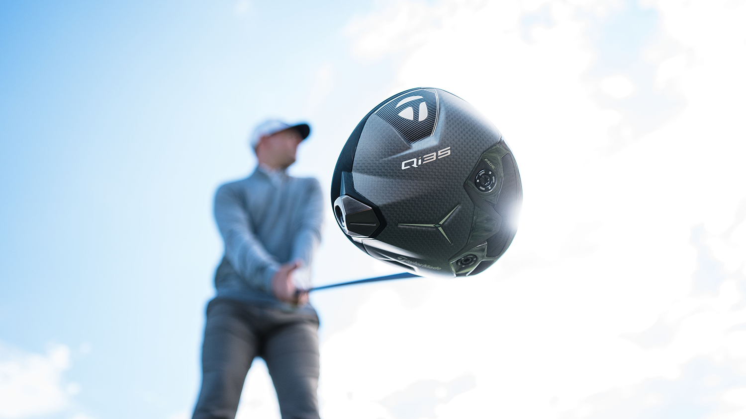 Golfspelare svingar en TaylorMade Qi10 golfklubba mot en ljusblå himmel, fokus på klubbhuvudet.