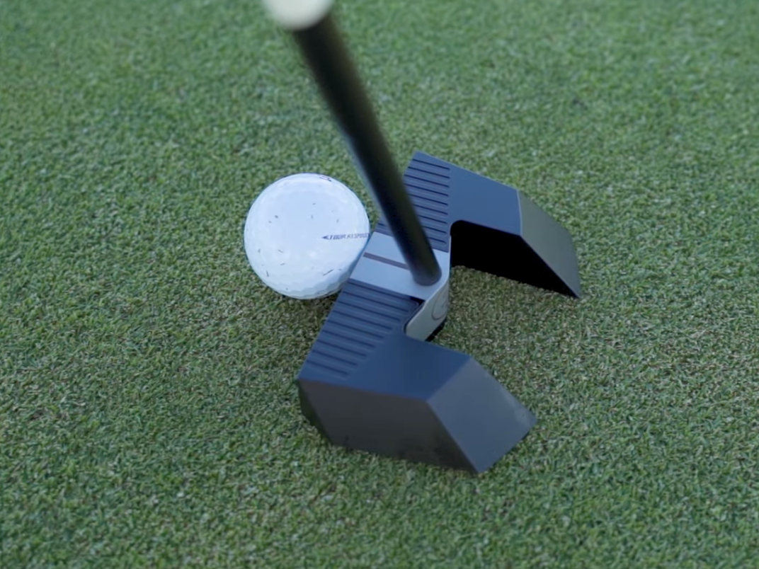 En golfboll ligger på greenen bredvid ett modernt svart putterhuvud som är redo att slå bollen.