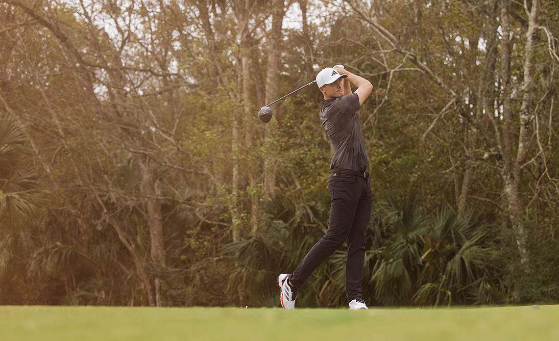 En golfspelare svingar en klubba på en grön golfbana omgiven av träd och växtlighet.