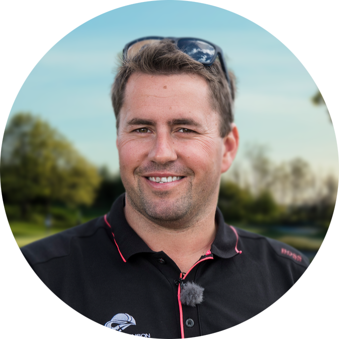 Man ler mot kameran, bär svart pikétröja med logotyp och solglasögon på huvudet, utomhus i grönskande parkmiljö.