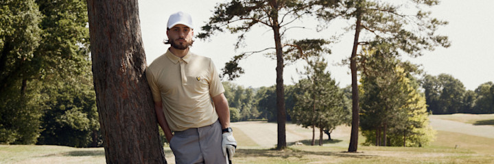 Young man holding a golf club and looking to the side on a golf course at sunset, with the Lyle & Scott Golf logo in the corner.