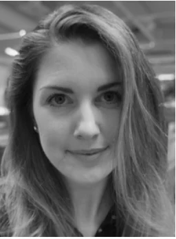 Kvinna med långt hår tittar rakt mot kameran i en inomhusmiljö med suddig bakgrund.