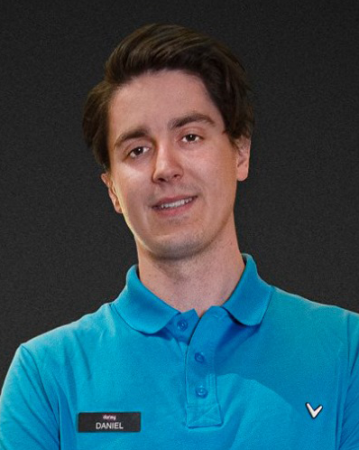 Man in a blue polo shirt with a name badge that says "Daniel" stands in front of a dark background, smiling slightly.