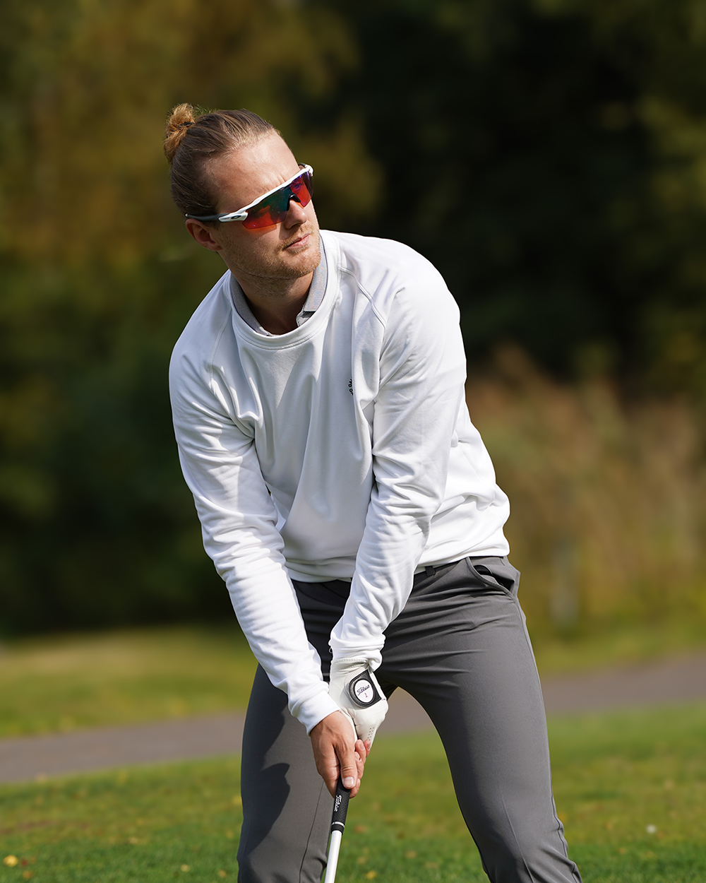 Man med solglasögon och vit tröja förbereder sig för att slå en golfboll på en grön golfbana utomhus.