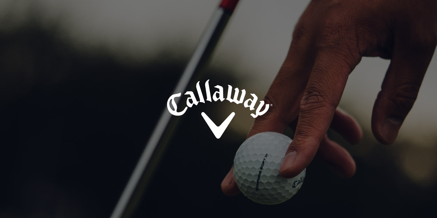 En hand placerar en Callaway-golfboll på marken bredvid en golfklubba, med Callaway-logotypen i mitten.