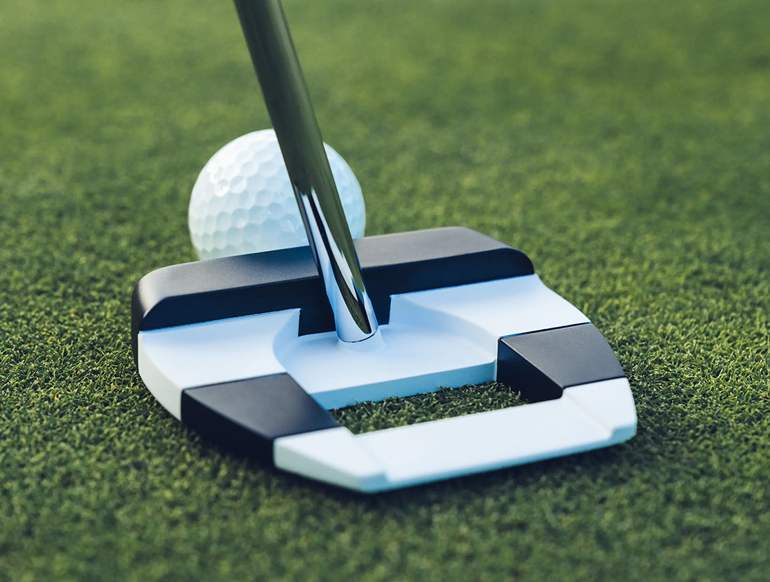 A golf club putts a golf ball on a well-manicured green lawn.