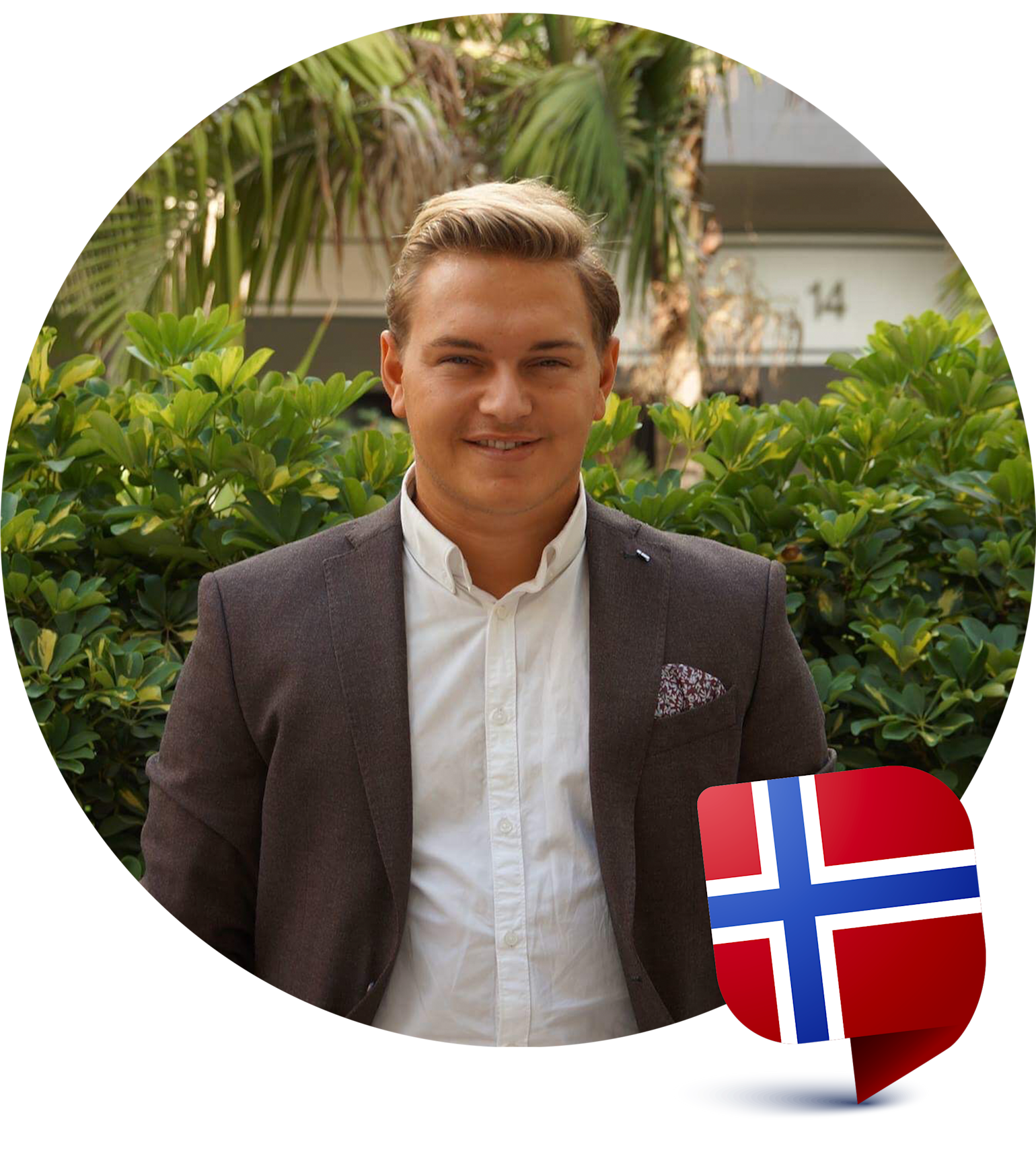 Man i kostym står framför gröna buskar och palmer, med en norsk flaggikon i nedre högra hörnet.