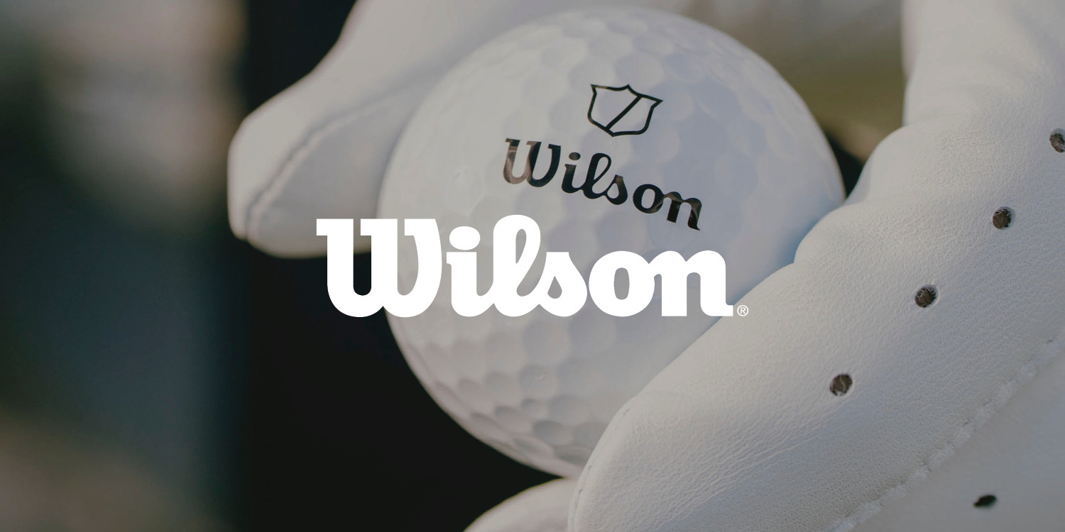 En vit golfboll med Wilson-logotyp hålls av en hand i vit golfhandske.