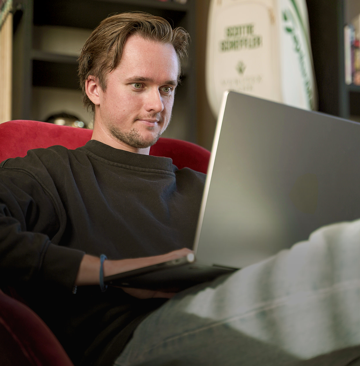 One sits relaxed in a red armchair, working on a laptop in a home office.