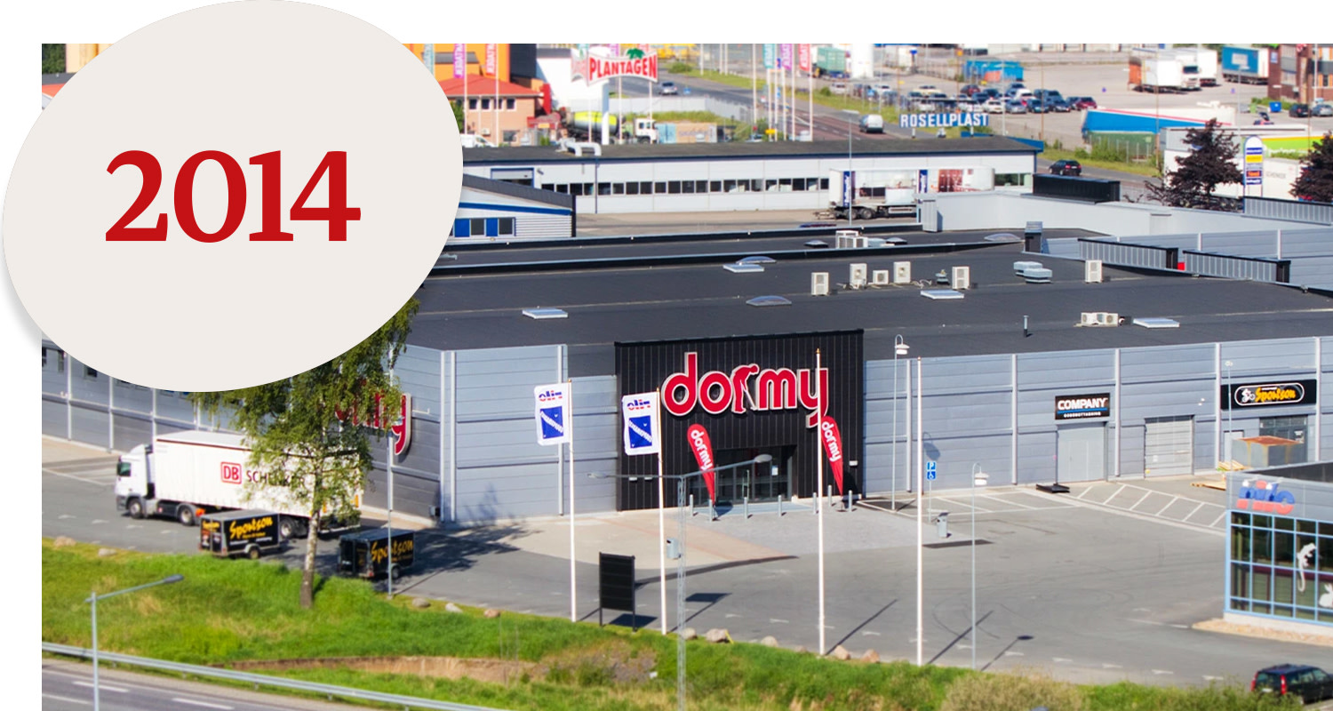 Large grey retail complex with a "dormy" sign and flags outside, large circle with the text "2014" in red.
