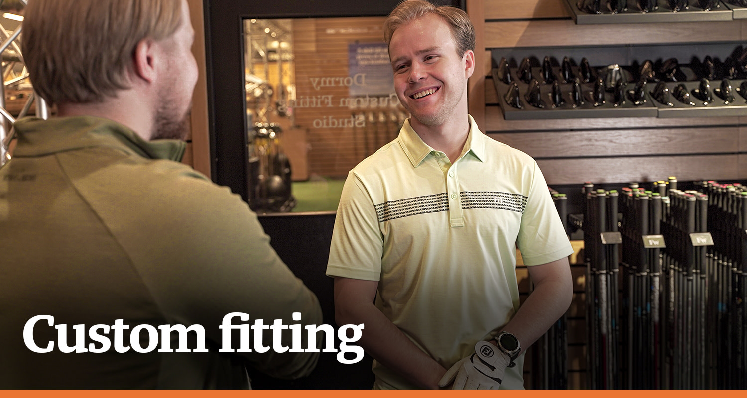 Två män samtalar och ler i en golfbutik, omgivna av golfklubbor och tillbehör, med texten "Custom fitting".