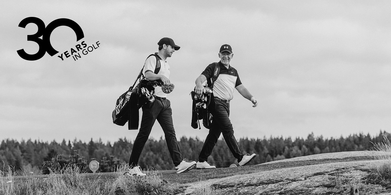 Two men are carrying golf bags and walking together on a golf course; a logo with the text "30 years in golf" is visible in the corner.
