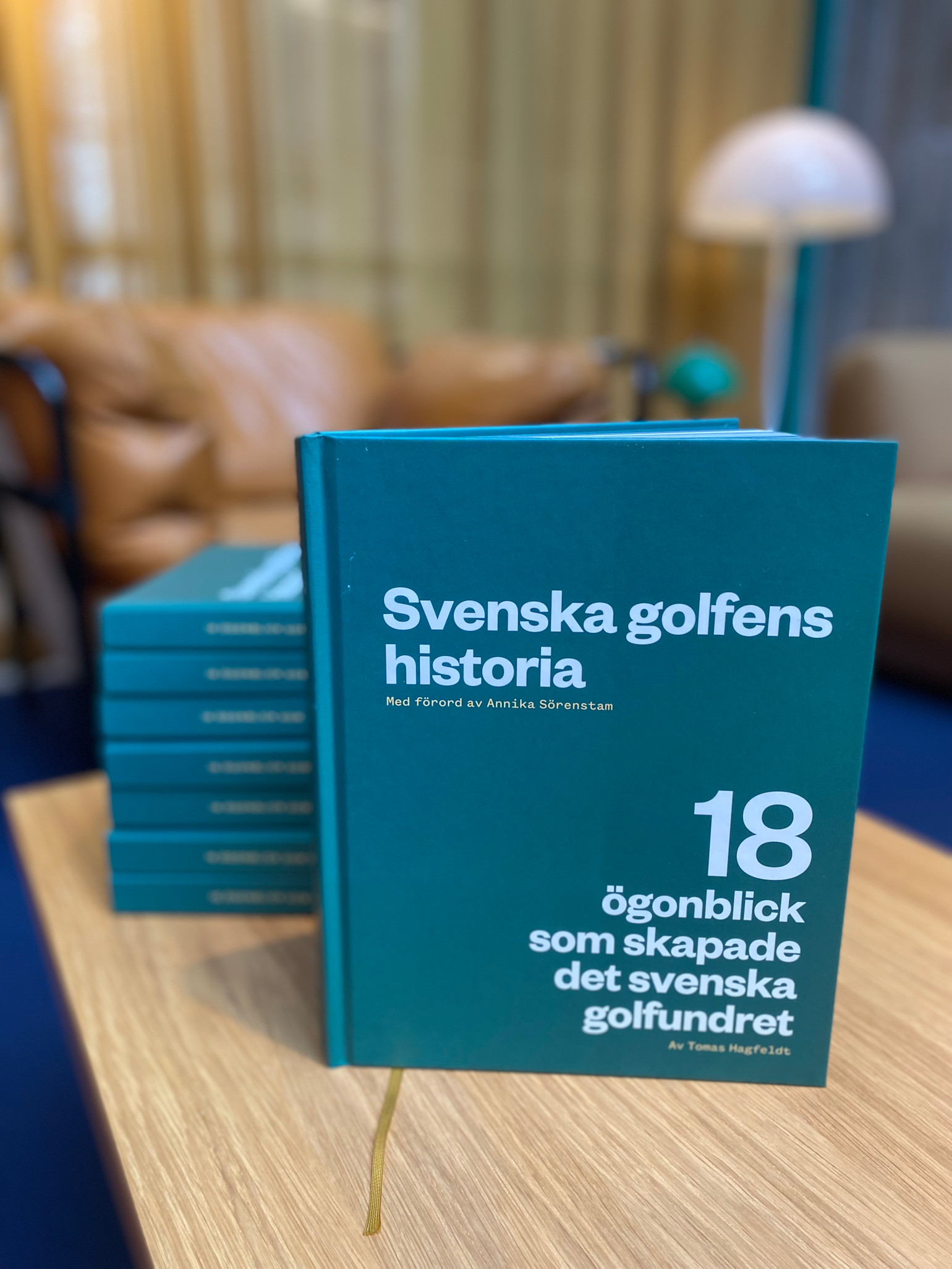Bok med titeln "Svenska golfens historia: 18 ögonblick som skapade det svenska golfundret" står på ett bord med fler exemplar i bakgrunden.